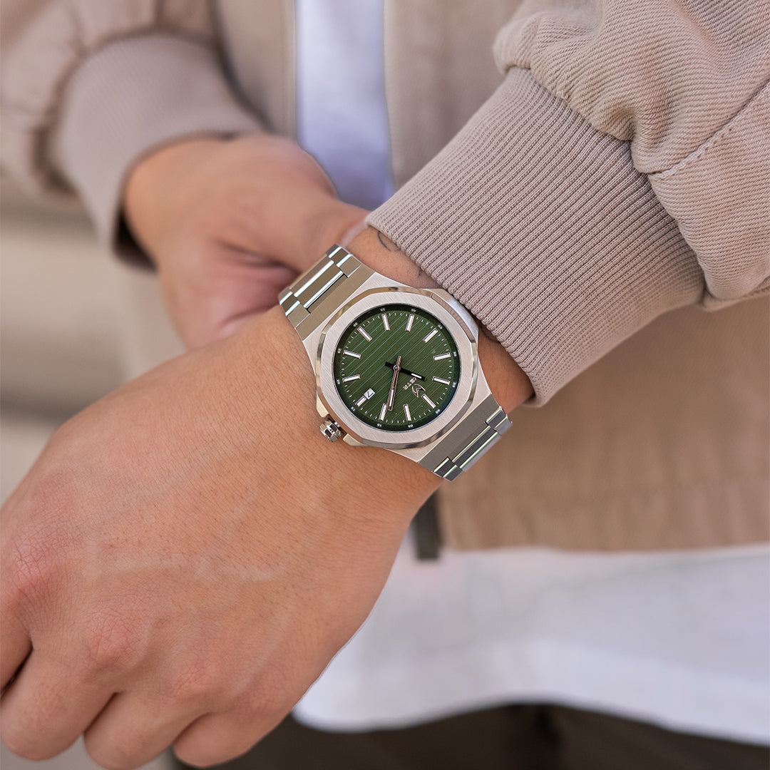silver watch on wrist with green dial